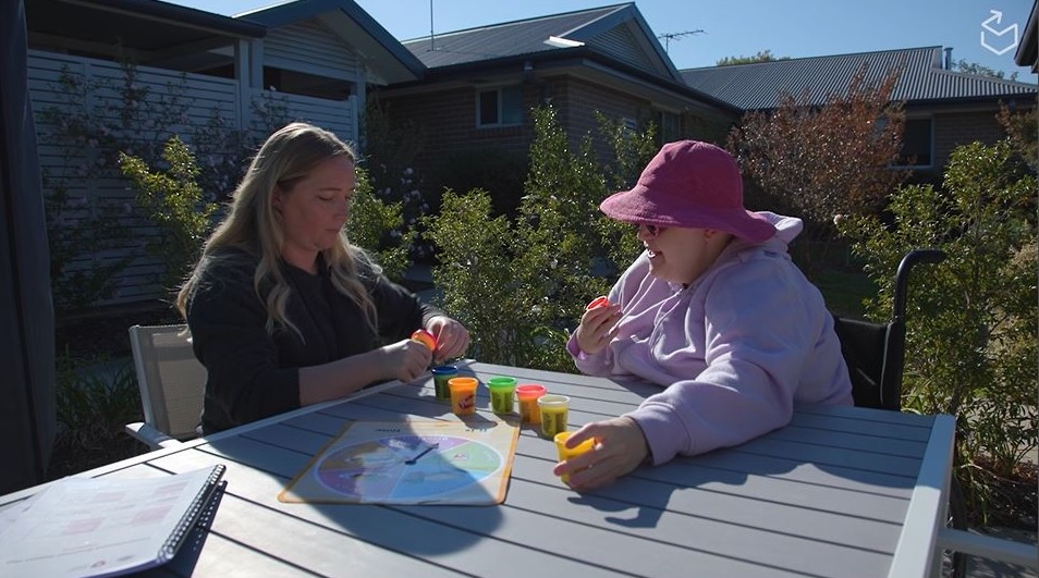 A support practitioner and person with disabilities sitting outside playing a board game.