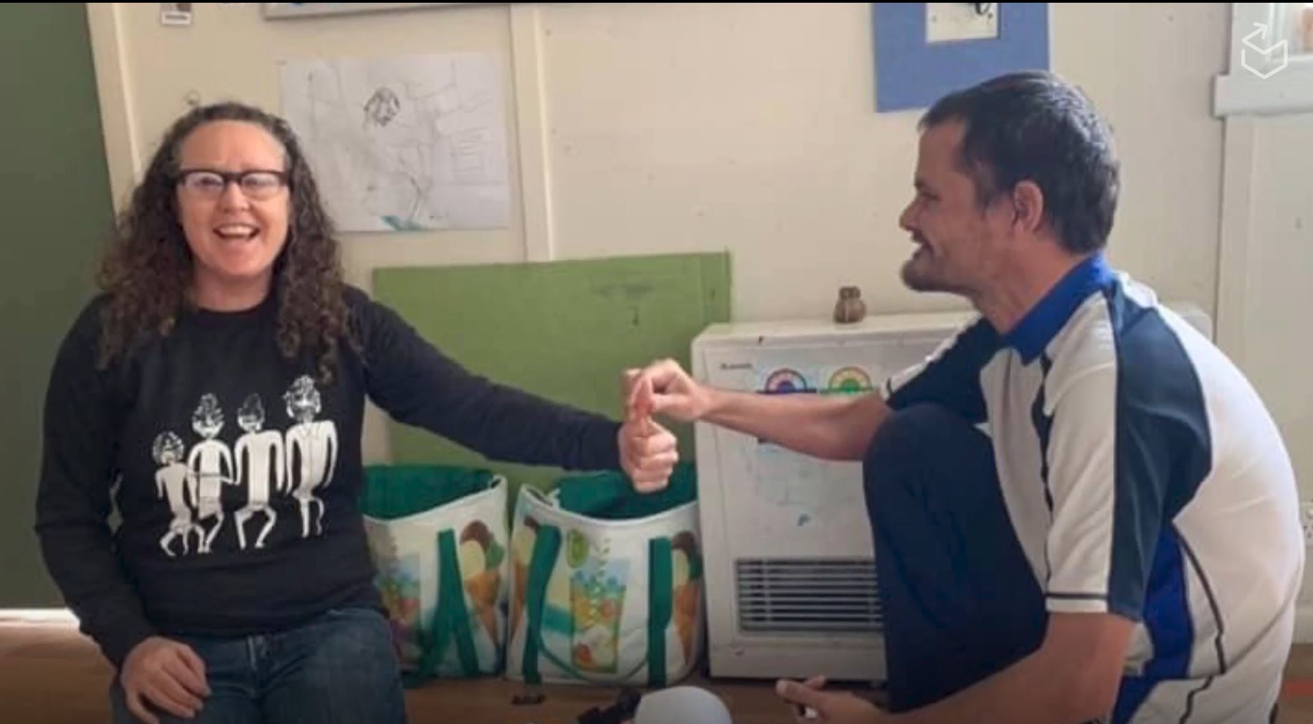 A support practitioner holds out their hand with their thumb up while a person with disabilities holds the thumb.