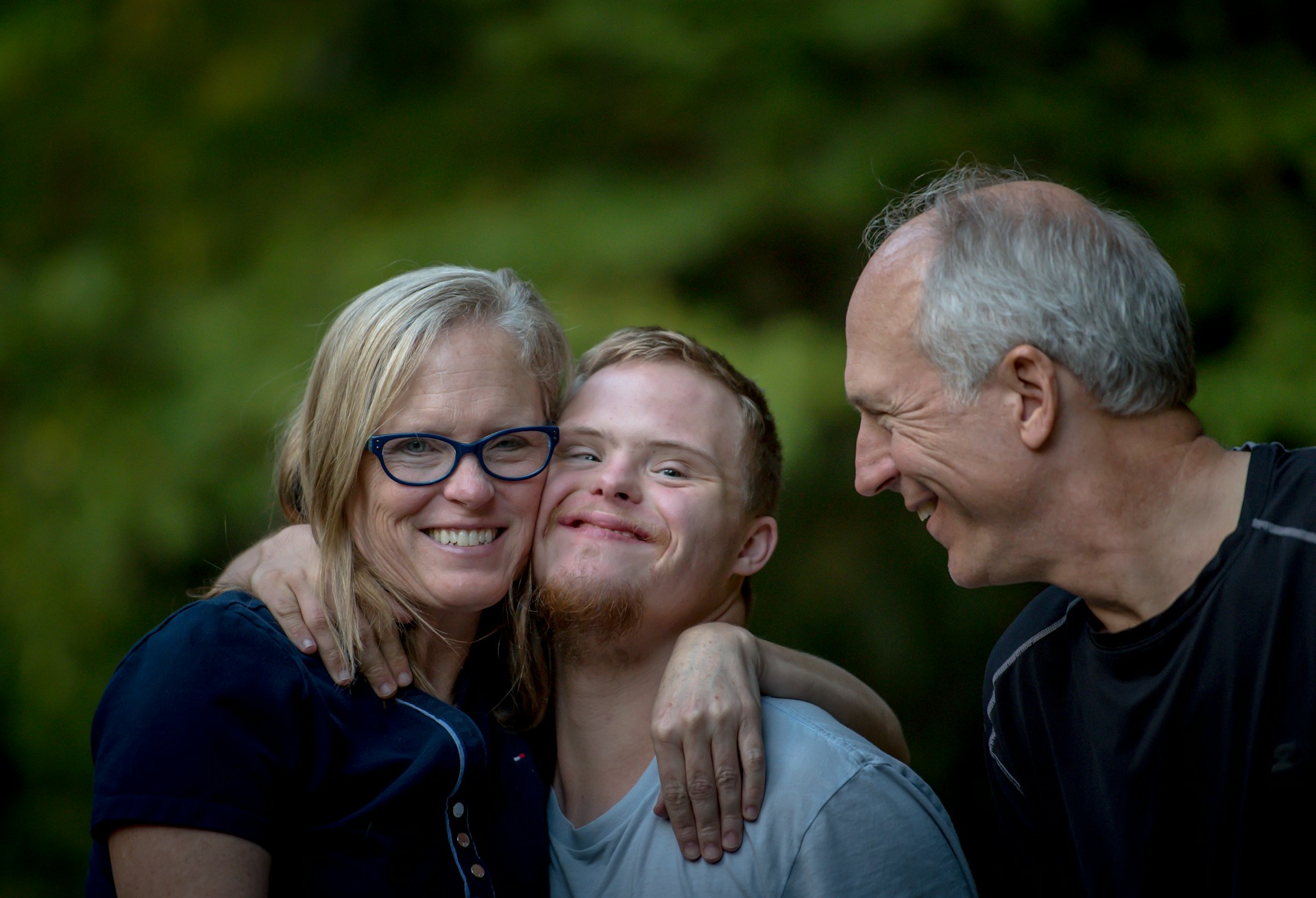 A person with disability is being hugged by a woman while a man smiles at them.