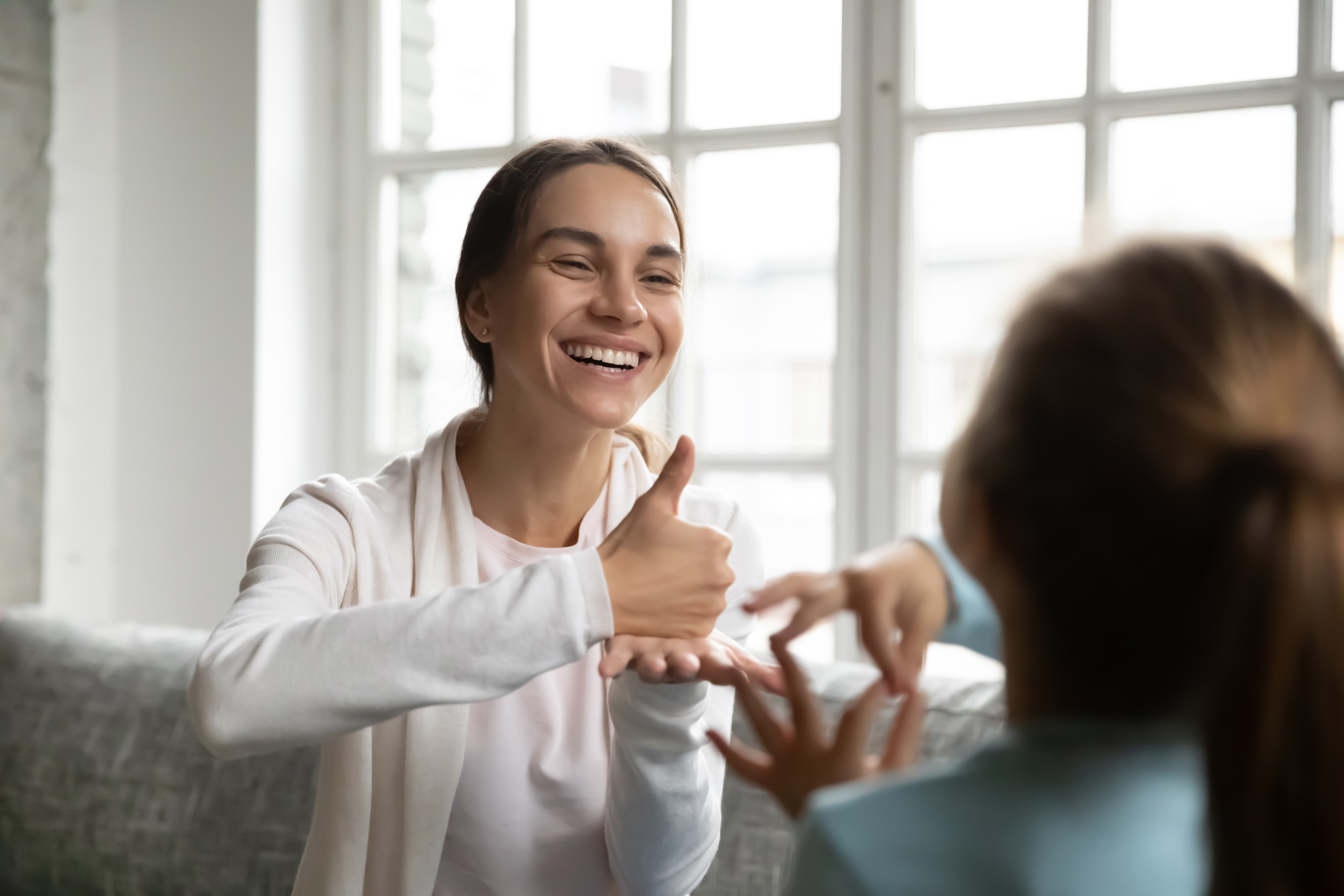 A woman smiles while using sign language to a child.